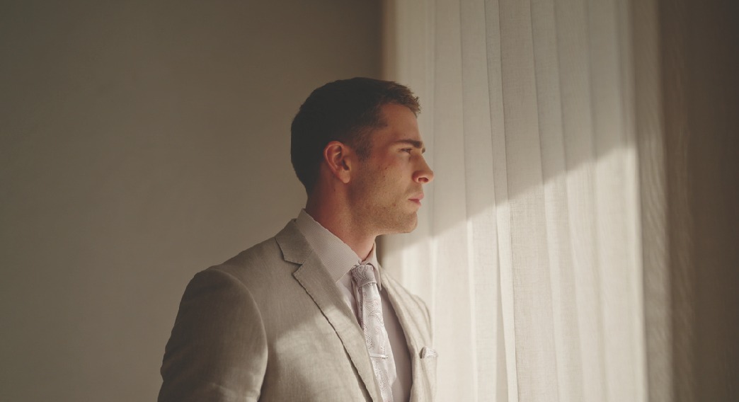 Man in a light suit by a window at sunset